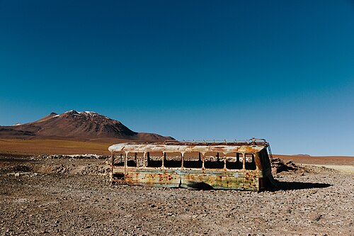 A rusted abandoned bus with missing windows in a desert landscape