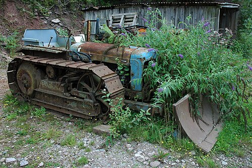 An abandoned tracked bulldozer with a front blade beside an old building