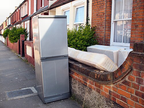 A discarded upright fridge-freezer standing on a pavement