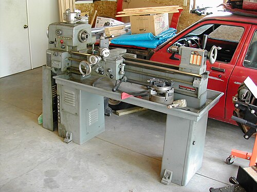A metalworking lathe with a long bed, handwheels and chuck in a workshop