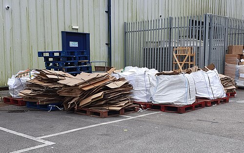 Flattened cardboard and bundled paper on pallets beside a recycling facility