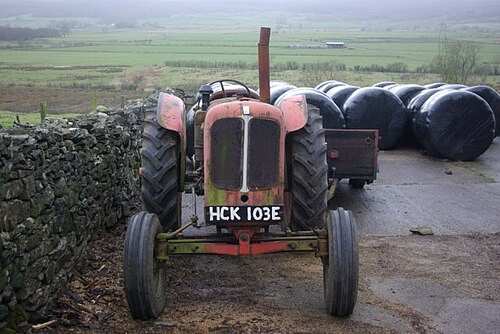 An older red farm tractor with large rear tyres parked beside a stone wall