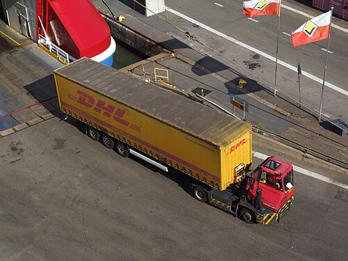 An articulated truck with a long yellow semi-trailer near a ferry terminal