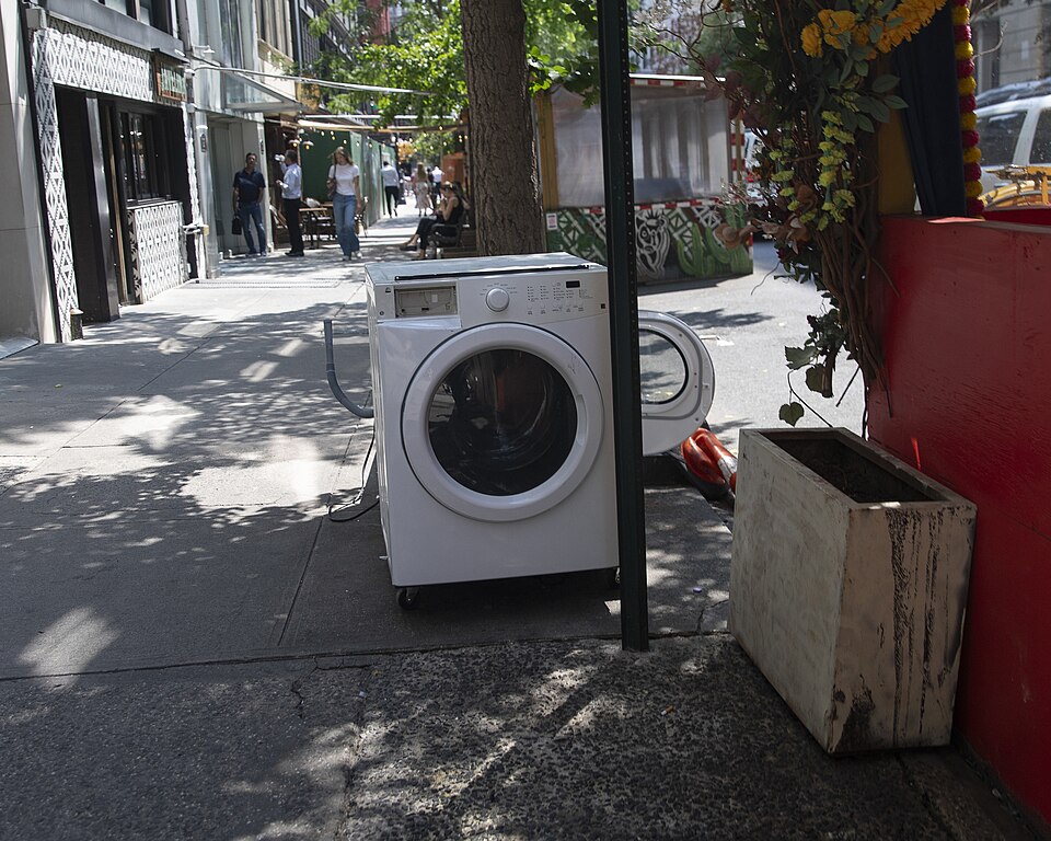 A discarded front-loading washing machine with its round door open